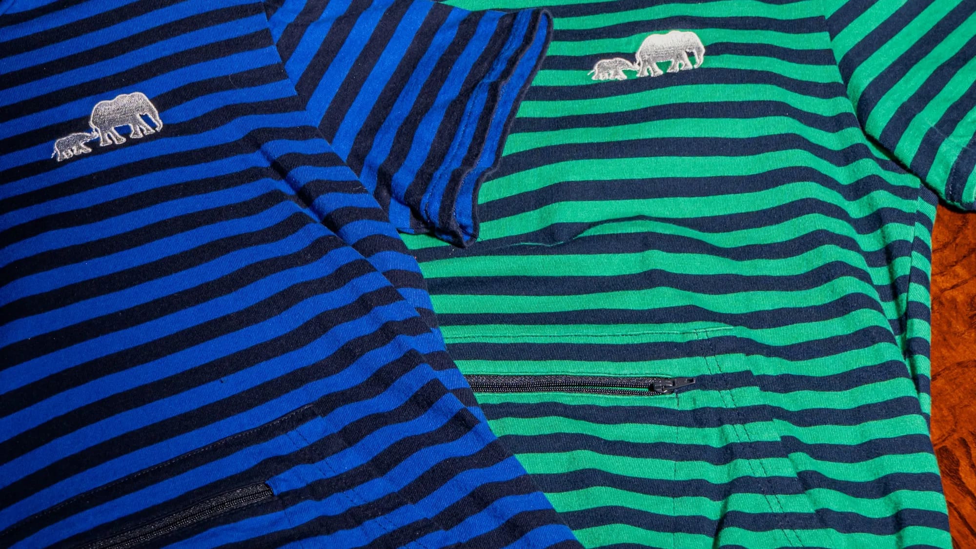 Blue and green striped hoodie tees folded together, the zipper pocket visible across each front