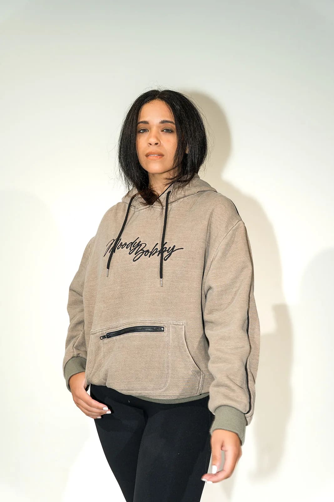 Woman in an oatmeal hoodie with her hand resting at the zipper pocket, framed from the nose down